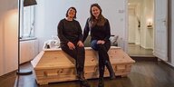 Sahra Ratgeber und Birgit Scheffler sitzen auf einem hellen Holzsarg