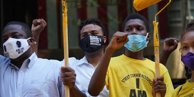 Aktivisten tragen Mundschutze und Stoffmasken und strecken ihre Fäuste nach oben während einer Protestaktion, in deren Rahmen der Schriftzug «Black Lives Matter» auf die Fifth Avenue vor dem Trump Tower gemalt wird.