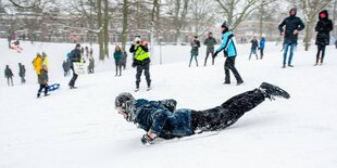 Winter in einem Park, Menschen sind im Schnee, ein Mann rodelt bäuchlings