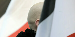 En Mann mit geschorenem Kopf steht zwischen schwarz-weiß-roten Fahnen während einer Demonstration von Rechtsextremen