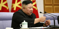 Kim Jong Un sitzt an einem Tisch und spricht in zwei Mikrofone. Vor ihm steht ein Teeservice.
