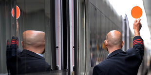 Ein Schaffner hebt am am Hauptbahnhof Hannover seine Kelle und zeigt dem Lokführer „Grün“ an