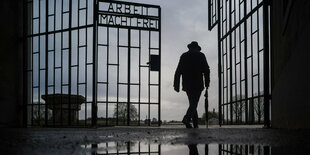 Die Silhouette eines Mannes der durch das Tor des Konzentrationslagers Sachsenhausen läuft - das Tor trägt die Inschrift "Arbeit macht frei"!