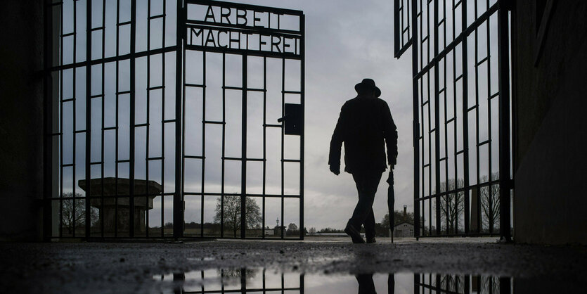 Die Silhouette eines Mannes der durch das Tor des Konzentrationslagers Sachsenhausen läuft - das Tor trägt die Inschrift "Arbeit macht frei"!