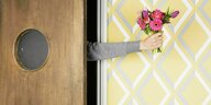 Eine Person streckt einen Blumenstrauss durch den Türspalt