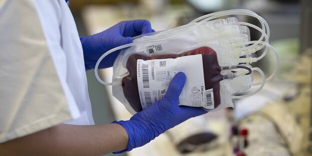 Eine Person mit Schutzhandschuhen trägt Blutkonserven