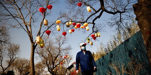 Ein Spaziergänger mit Mundschutzmaske und ein mit roten und gelben Lampions geschmückter Baum