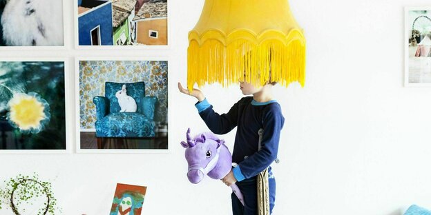Ein Junge steht unter einem gelben Lampenschirm mit Fransen in seinem Kinderzimmer