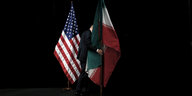 Ein Mann trägt die Iranische fahne von einer Bühne - daneben steht die US-amerikanische Flagge