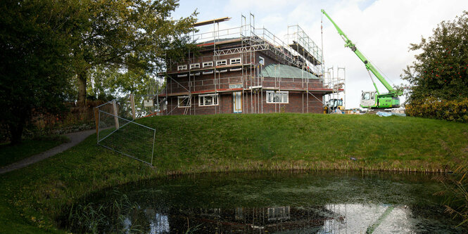 Ein Haus im Bau hinter einem trüben Fischteich
