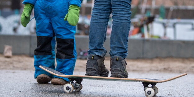 Man sieht Kinder im Schneeanzug und auf dem Skateboard
