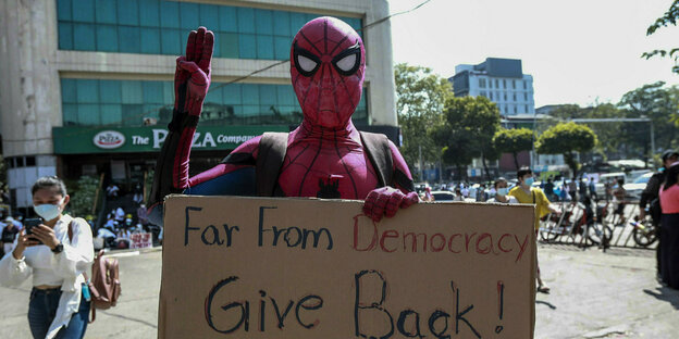ein als Spiderman verkleideter Demonstrant hält ein Protestschild und eine Hand mit drei Fingern, das Zeichen der Bewegung, hoch