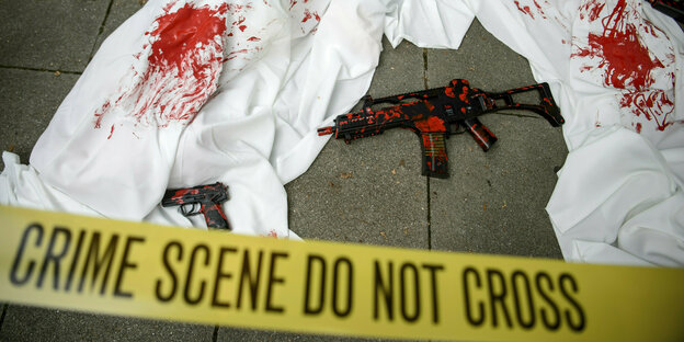 Waffenatrape und mit Kunstblut versehene Kleidung liegen am rande einer Protestaktion auf der Straße