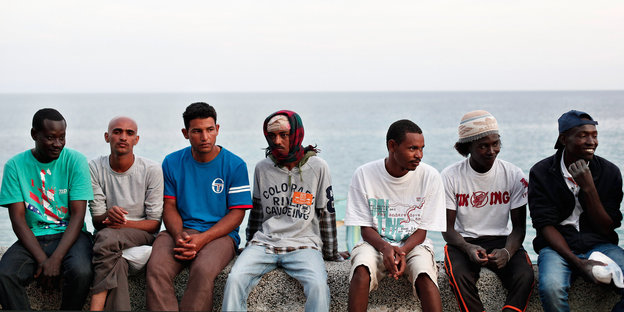 Flüchtlinge sitzen auf einer Mauer vorm Mittelmeer