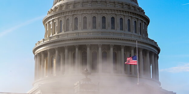 Die Kuppel des Kapitols in Washington mit Dampf und US-Flagge im Vordergrund