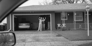 Ein älteres Paar winkt vor der Garage stehend