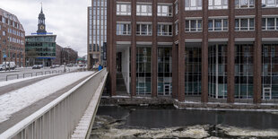 Backsteingebäude mit großen Fenstern an einer Brücke, darunter Eisschollen