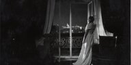 Szene aus dem Film „Tagebuch der Geliebten“: Eine Frau im Nachthemd lehnt mit dem Rücken zur Kamera an einem Fenster und blickt hinaus