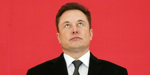 Elon Musk blickt nach oben vor einem roten Hintergrund