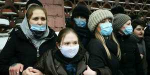 Junge Menschen mit Gesichtsmasken untergehakt während einer Demonstration