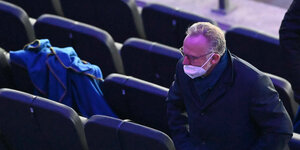 Karl-Heinz Rummenigge mit schlecht sitzender OP-Maske auf der TZribüne eines Stadion