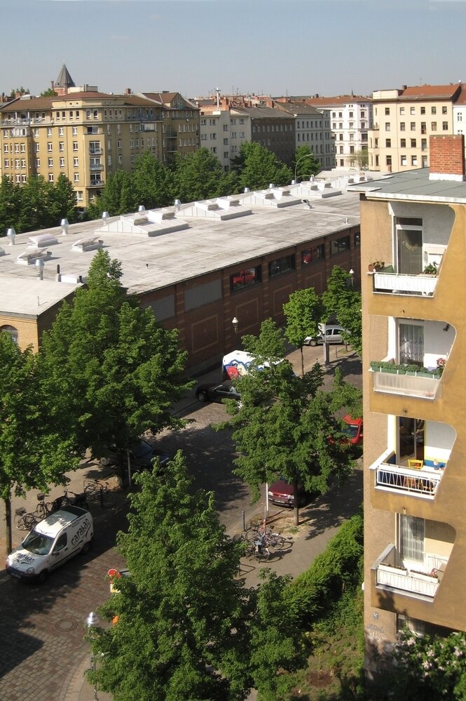 Das Bild zeigt den Blick aus dem Fenster über die Marheineke-Markthalle in Berlin. Man sieht Häuserfronten und einen Parkplatz.