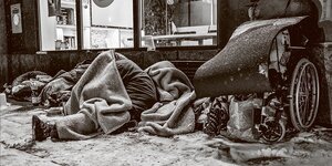 Obdachlose liegen und sitzen unter zugeschneiten Decken und Isomatten.