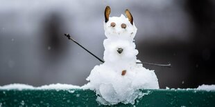 Auf der Lehne einer Parkbank ist ein kleiner Schneemann