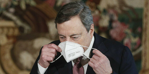 Mario Draghi nimmt gerade seinen Nasen-/Mundschutz aus seinem Gesicht