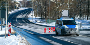 Auf einer winterlichen Straße parkt ein Polizeifahrzeug, Auf der Fahrbahn sind rote Warnschilder platziert