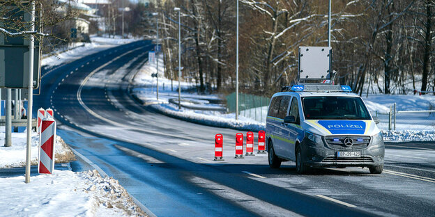 Auf einer winterlichen Straße parkt ein Polizeifahrzeug, Auf der Fahrbahn sind rote Warnschilder platziert