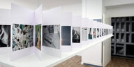 Ausstellungsansicht aus "Revision: Peripherie als Ort. Das Hellersdorf-Projekt": Ein Faltbuch mit bunten Fotos von Ulrich Wüst steht auf einer Platte, die von der Decke schwebt