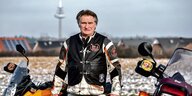 Heli Lill trägt die Lederjacke seines Motorrad-Clubs und steht zwischen zwei Motorrädern.