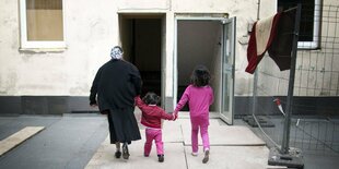 Eine Frau mit zwei Kindern an der hand läuft in eine Mehrfamilienhaus