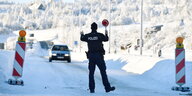 Ein Polizist mit Kelle fordert ein sich näherndes Auto in winterlicher Landschaft zum Anhalten auf