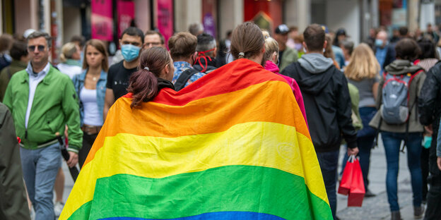 Zwie Menschen mit einer Regenbogenflagge über den Schultern laufen durch München