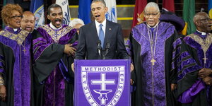 Barack Obama an einer Kanzel, hinter ihm Pastoren