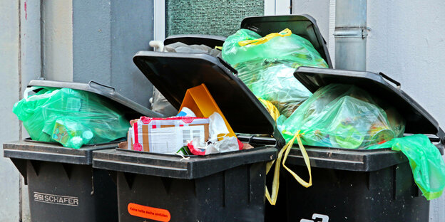 Grüne Müllbeutel quellen aus Mülltonnen.