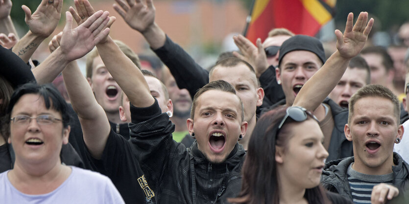 Eine größere Gruppe von Menschen. Sie demonstrieren und strecken die Arme hoch.