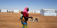 Eine Frau mit Kleinkind auf dem Rücken läuft durch ein Camp für Geflüchtete aus der Sahel Region in Dori, Burkina Faso