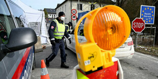 Ein Polizist an einem Grenzschild, im Vordergrund die Warnlampe einer Absperrung