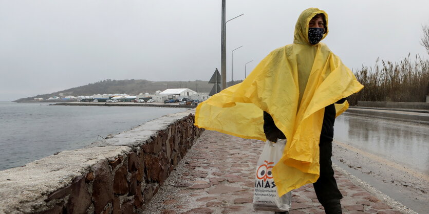 Eine Person in gelber Regenjacke, im Hintergrund ein Zeltlager