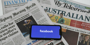 Ein Smartphone mit Facebook-Logo liegt auf einem Stapel australischer Zeitungen
