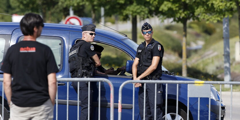 Zwei französische Polizisten stehen vor einem Polizeiauto.