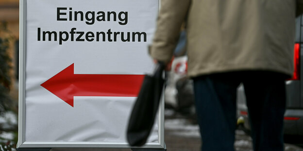 Ein Schild vor dem Impfzentrum in Halle/Saale weist den Weg zum Eingang - im Vordergrund ein Mann mit Tasche