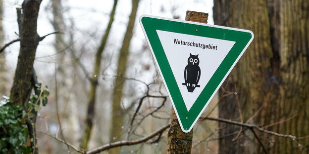 Naturschutzgebiet-Schild steht etwas schräg zwischen Bäumen