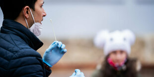 Ein Lehrer demonstriert Schülern die Handhabung eines Antigen-Schnelltests mit langem Wattestäbchen in der Hand