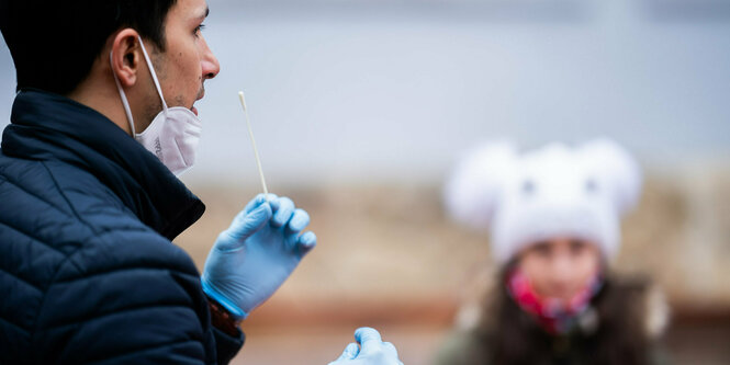 Ein Lehrer demonstriert Schülern die Handhabung eines Antigen-Schnelltests mit langem Wattestäbchen in der Hand