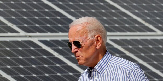 Joe Biden mit Sonnenbrille läuft vor Solar-Panelen