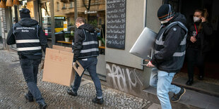 Polizisten tragen bei der Großrazzia Kisten aus einem Haus in Neukölln